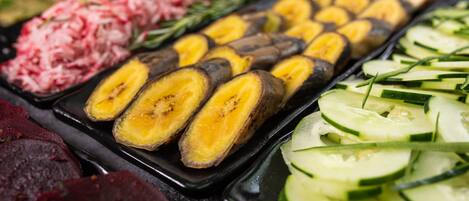 Variedades de vegetais e frutas cortadas, incluindo pepinos, bananas e beterrabas, dispostas numa bandeja.