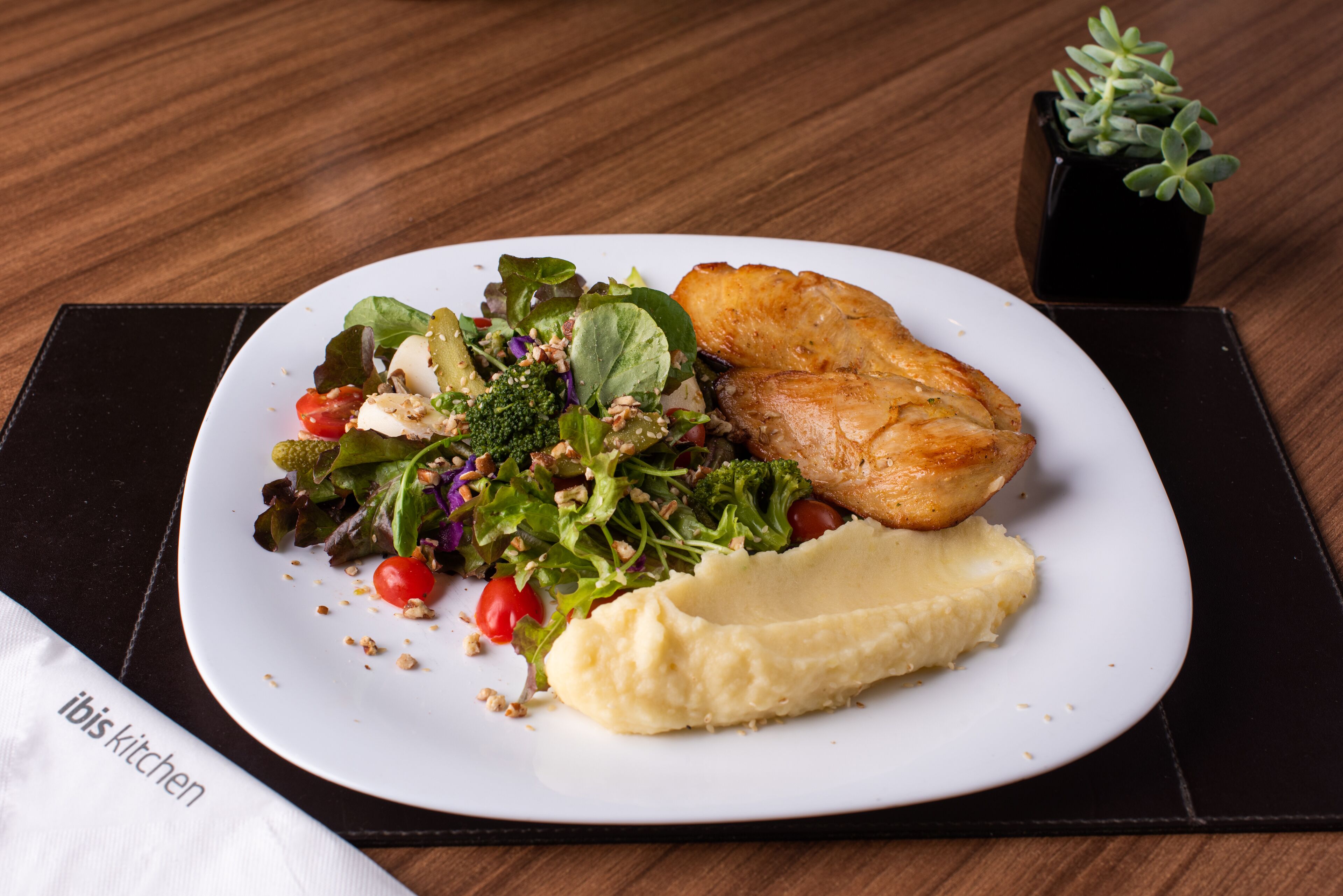 A plate with a salad, mashed potatoes, and a piece of meat on a wooden table.