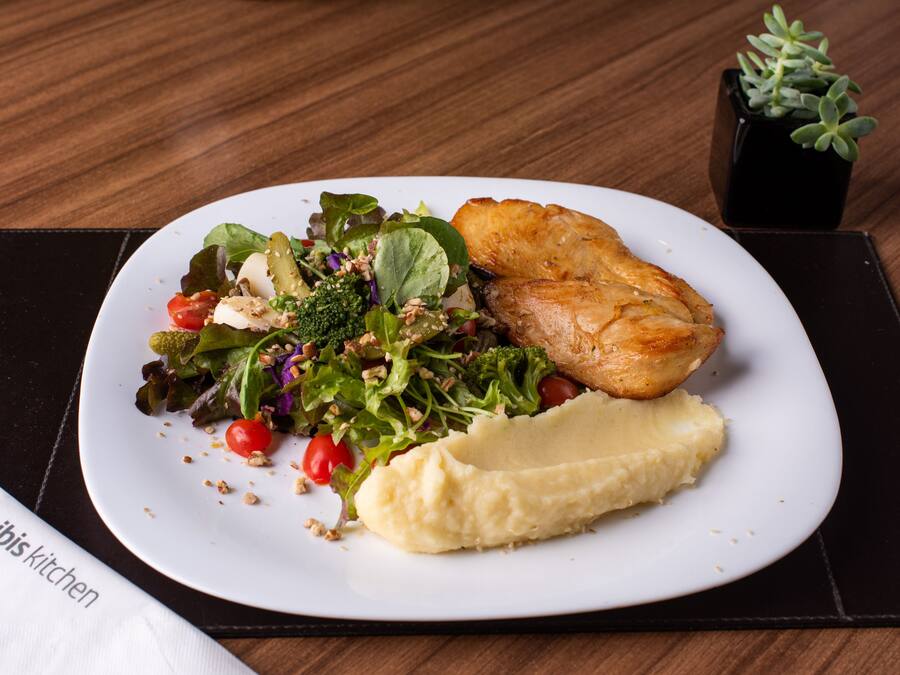 A plate with a salad, mashed potatoes, and a piece of meat on a wooden table.