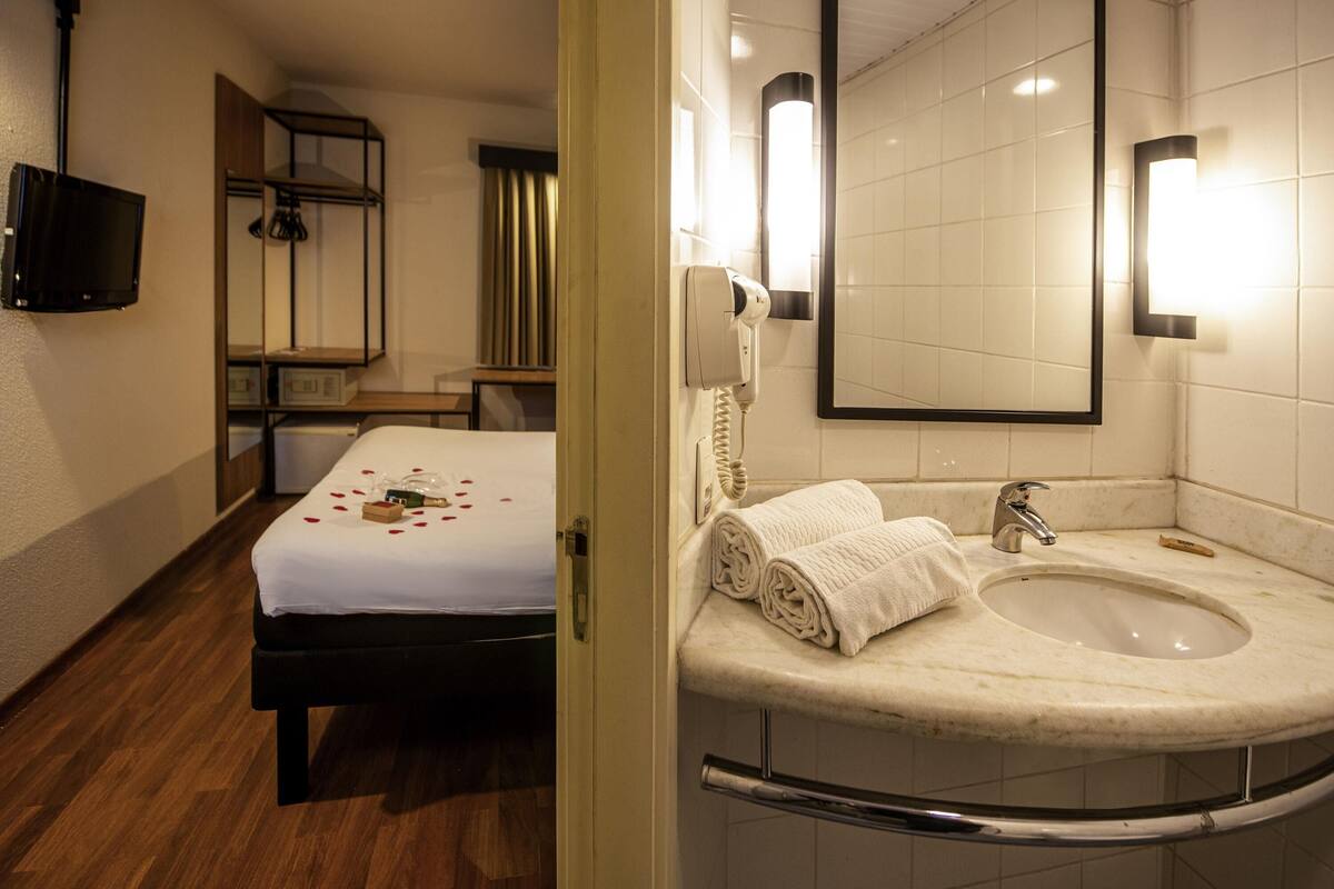 A hotel room with a bed, a bathroom with a sink and mirror, and a television mounted on the wall.