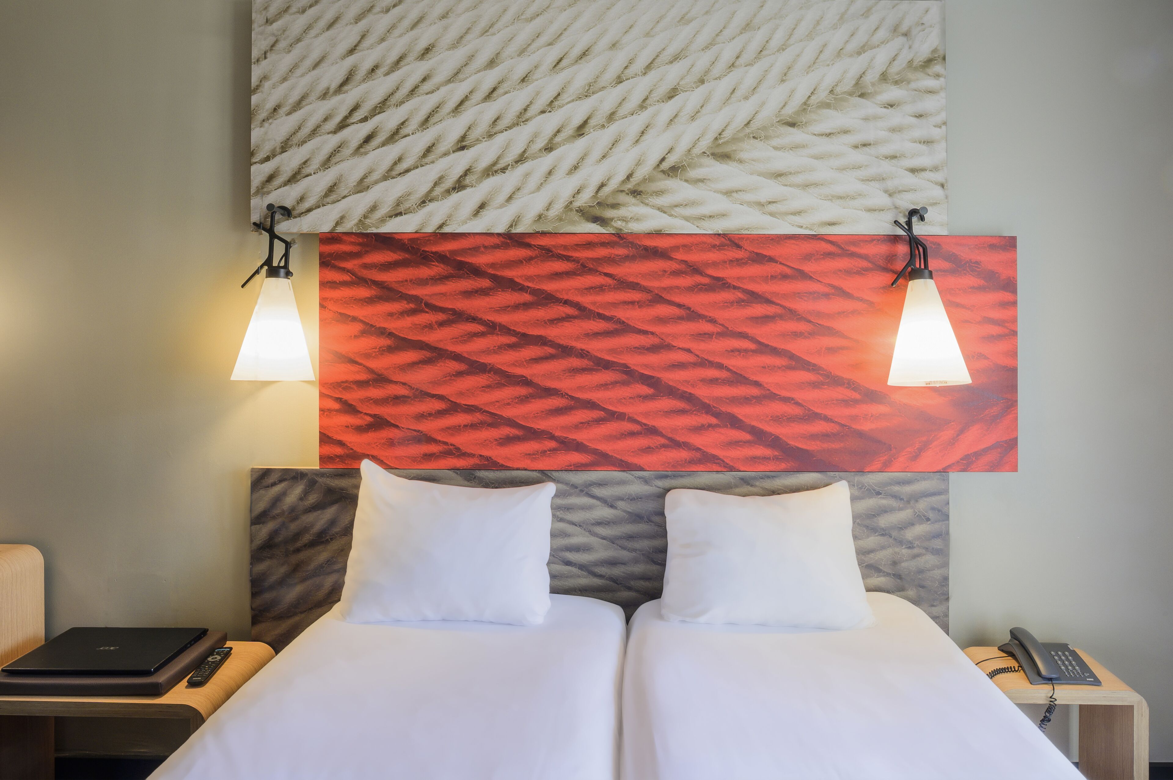 Een hotelkamer met twee bedden, een nachtkastje met een lamp, een telefoon en een laptop.