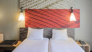 Ein Hotelzimmer mit zwei Betten, einem Nachttisch mit Lampe, Telefon und Laptop.