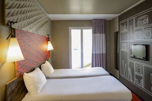 Una habitación de hotel con una cama, dos lámparas de noche, un televisor y un ventanal con cortinas.