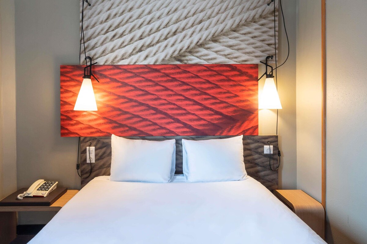 Een hotelkamer met een bed, twee bedlampen, een telefoon en een wand met een structuur.
