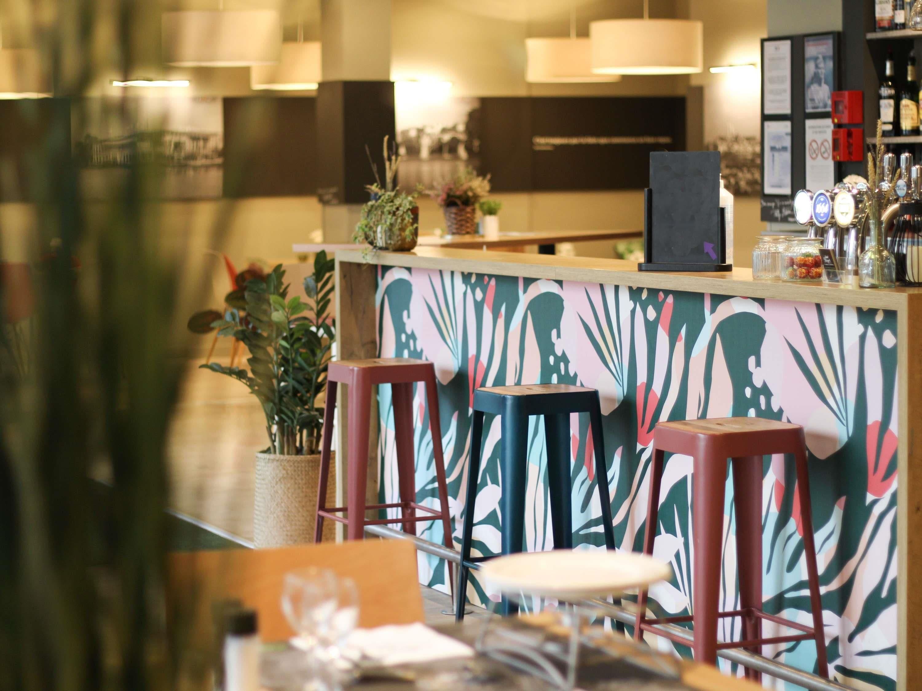 Een bar met krukken, een toonbank en een decoratieve wand.