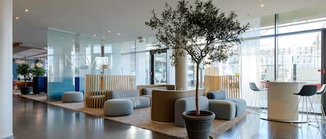 Un vestíbulo moderno con un gran árbol en maceta, zonas de estar y un muro de cristal con señalización.