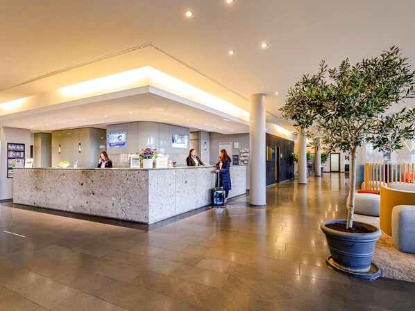 Un moderno vestíbulo de hotel con una recepción, un área de descanso y una gran planta en maceta.