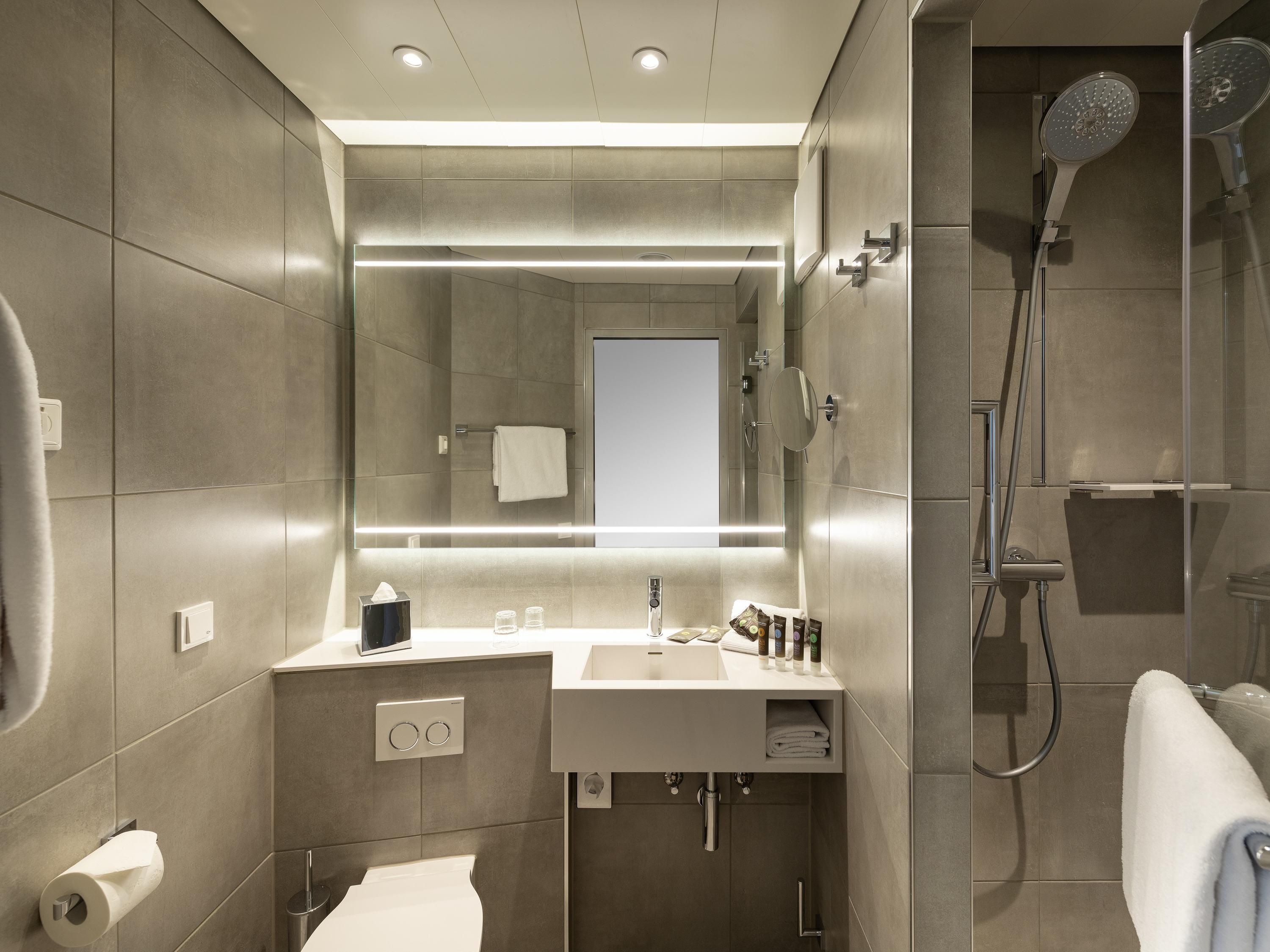 A modern bathroom with a large mirror, a sink, a shower, and a toilet.