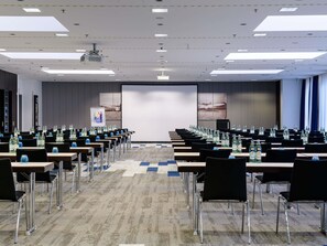 Ein Konferenzraum mit Tischen und Stühlen, einer Projektionsleinwand und einem großen Fenster.