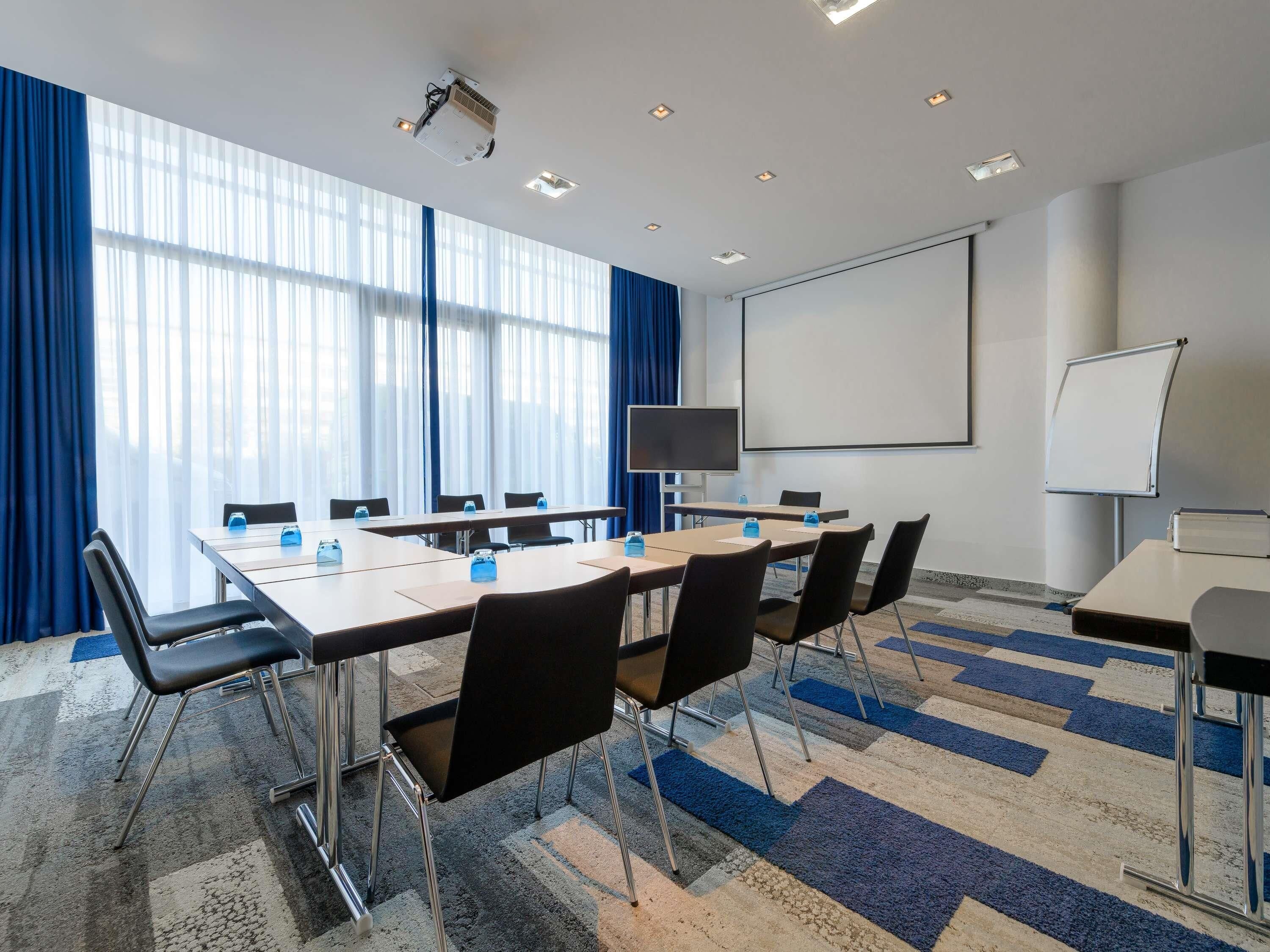 A conference room with a large table, chairs, a projector, a screen, and a whiteboard.