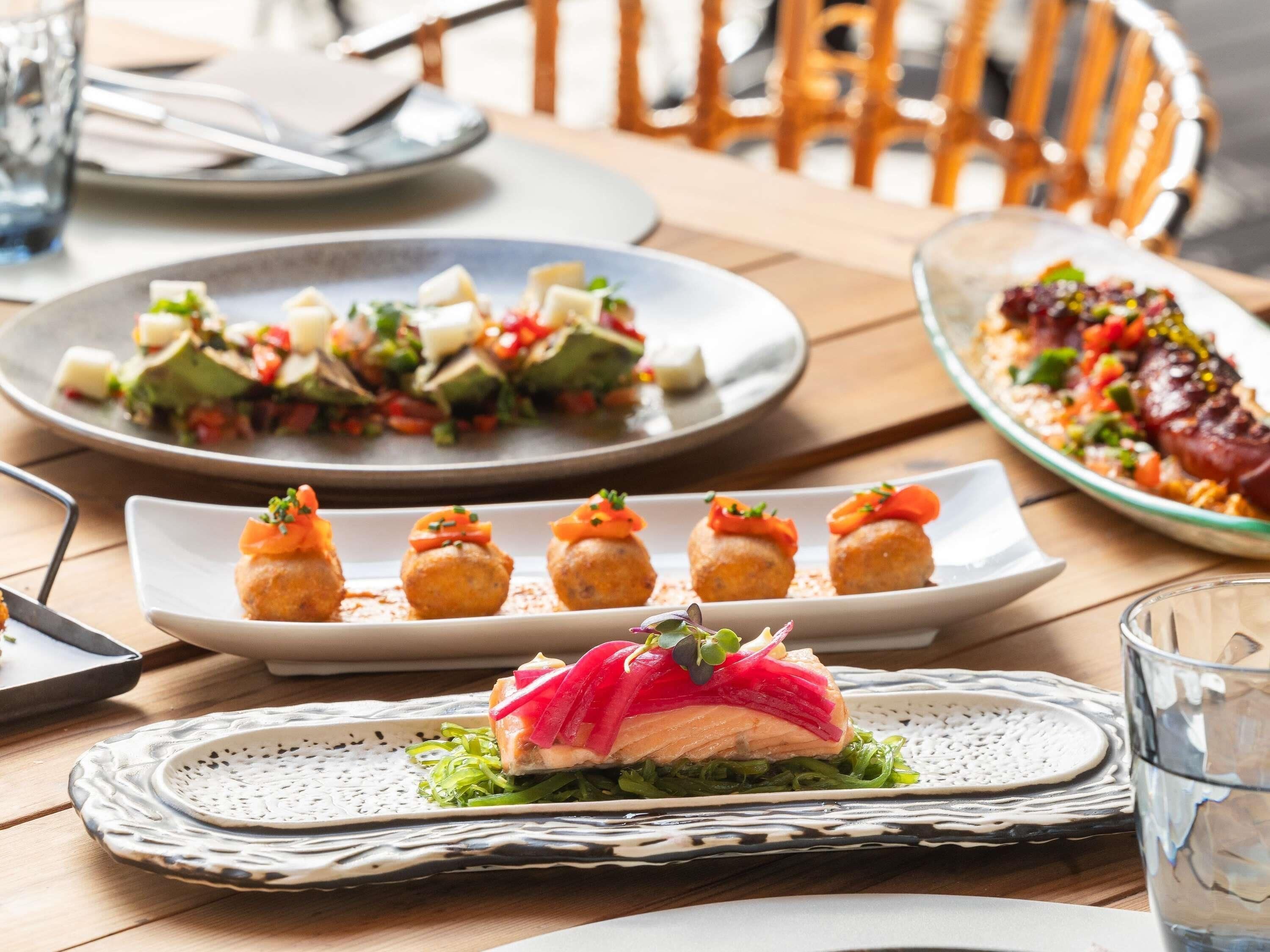 A dining table with various dishes, including a plate of appetizers, a dish with salmon and greens, and a plate with a salad.