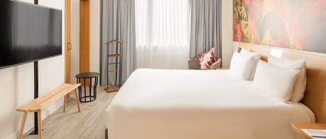 A hotel room with a large bed, a flat-screen TV, a wooden bench, a small table, and a painting on the wall.