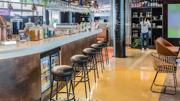 Zona de bar moderna con una barra larga, taburetes y una variedad de botellas y tarros en estantes.