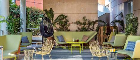 A modern outdoor seating area with green sofas, wicker chairs, and a hanging chair.