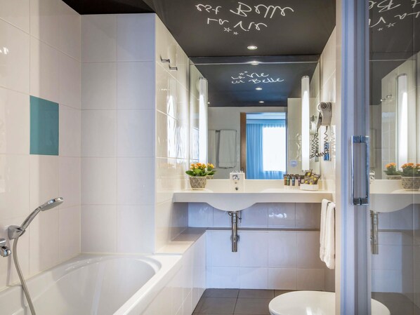 A modern bathroom with a bathtub, toilet, and a large mirror. - Novotel Barcelona Cornella (Cornella de Llobregat)