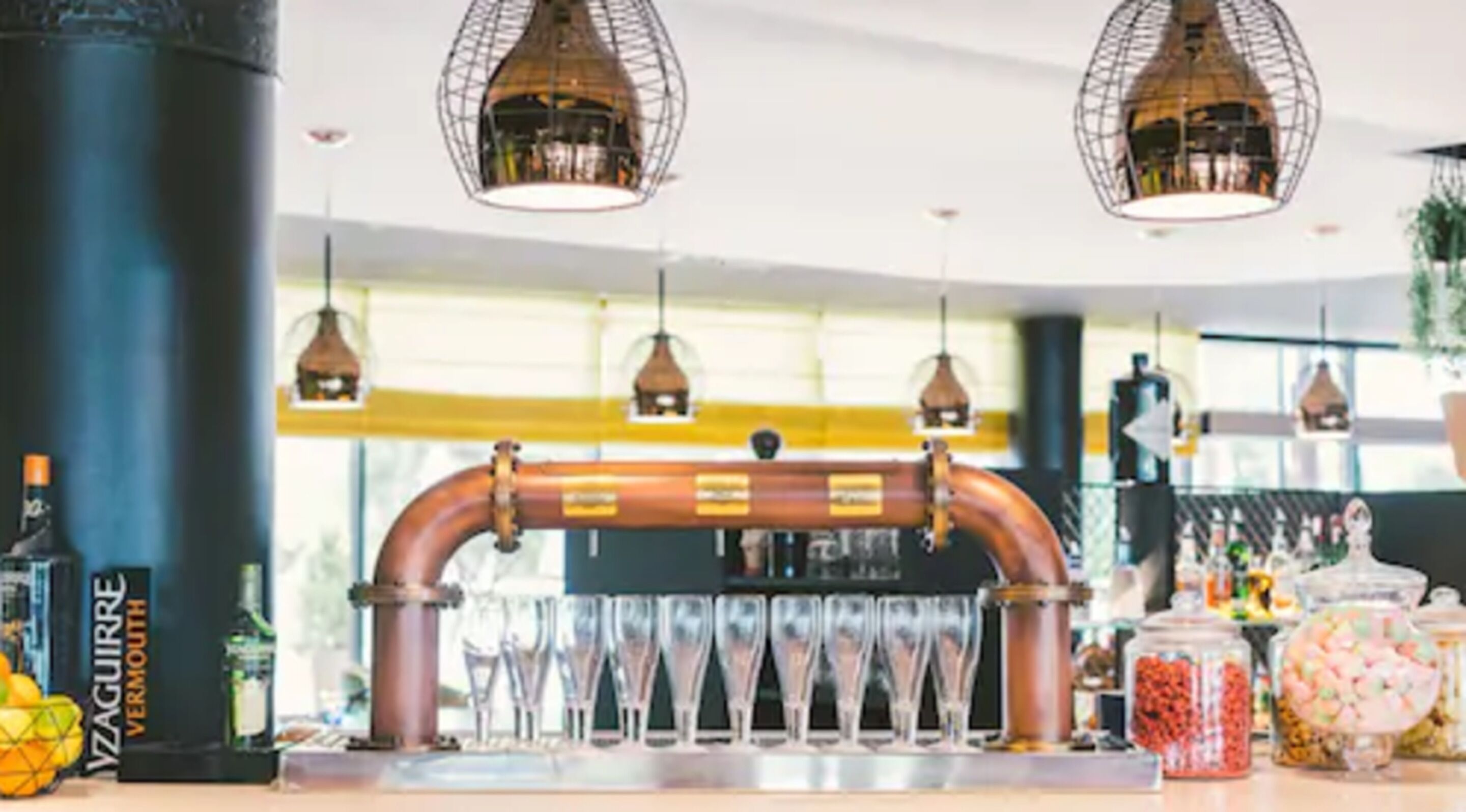 Una zona de bar con cañerías de cobre, vasos y diferentes botellas.