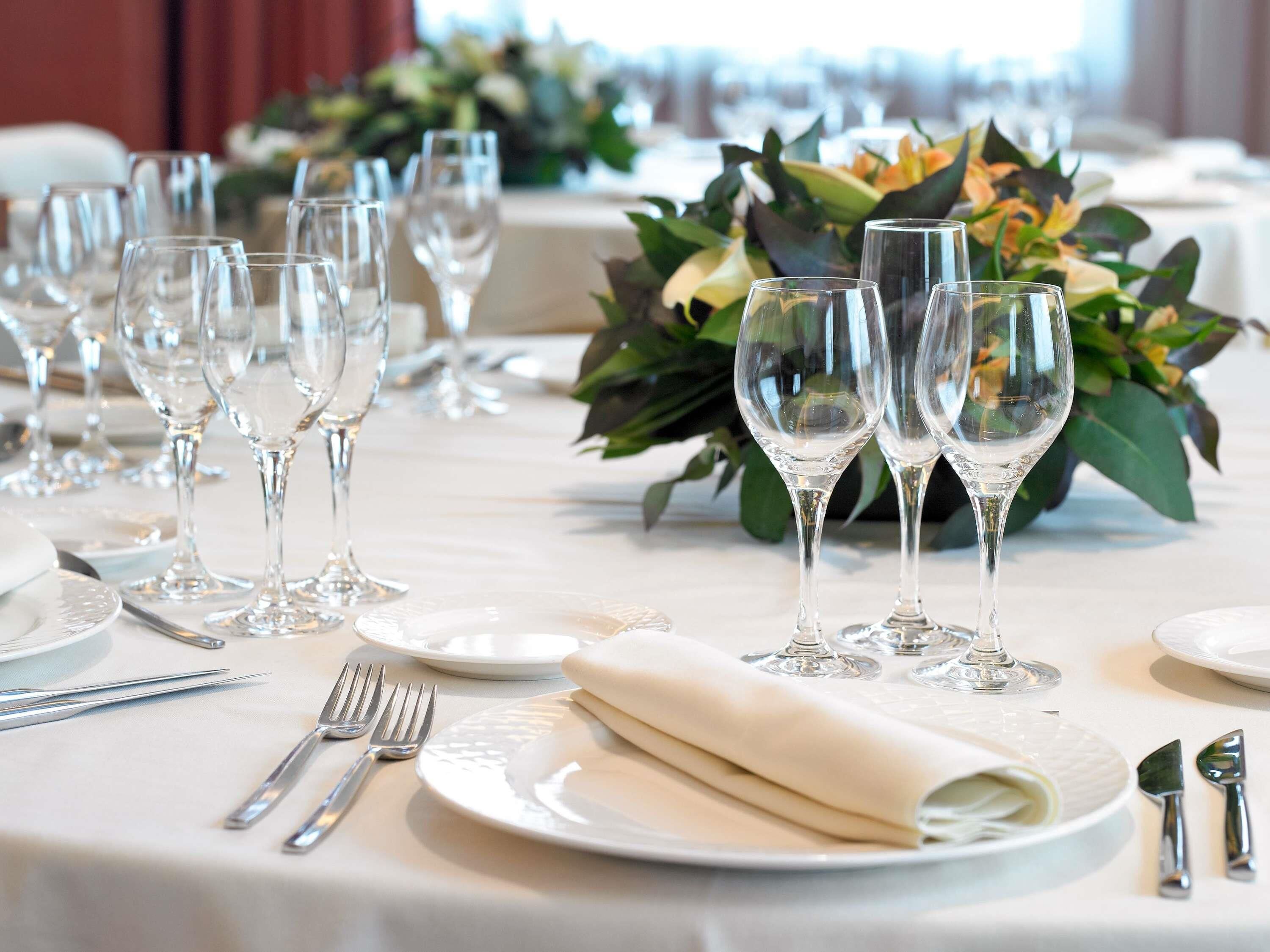 Mesa posta para um evento de jantar formal, com vários copos de vinho, pratos e talheres.