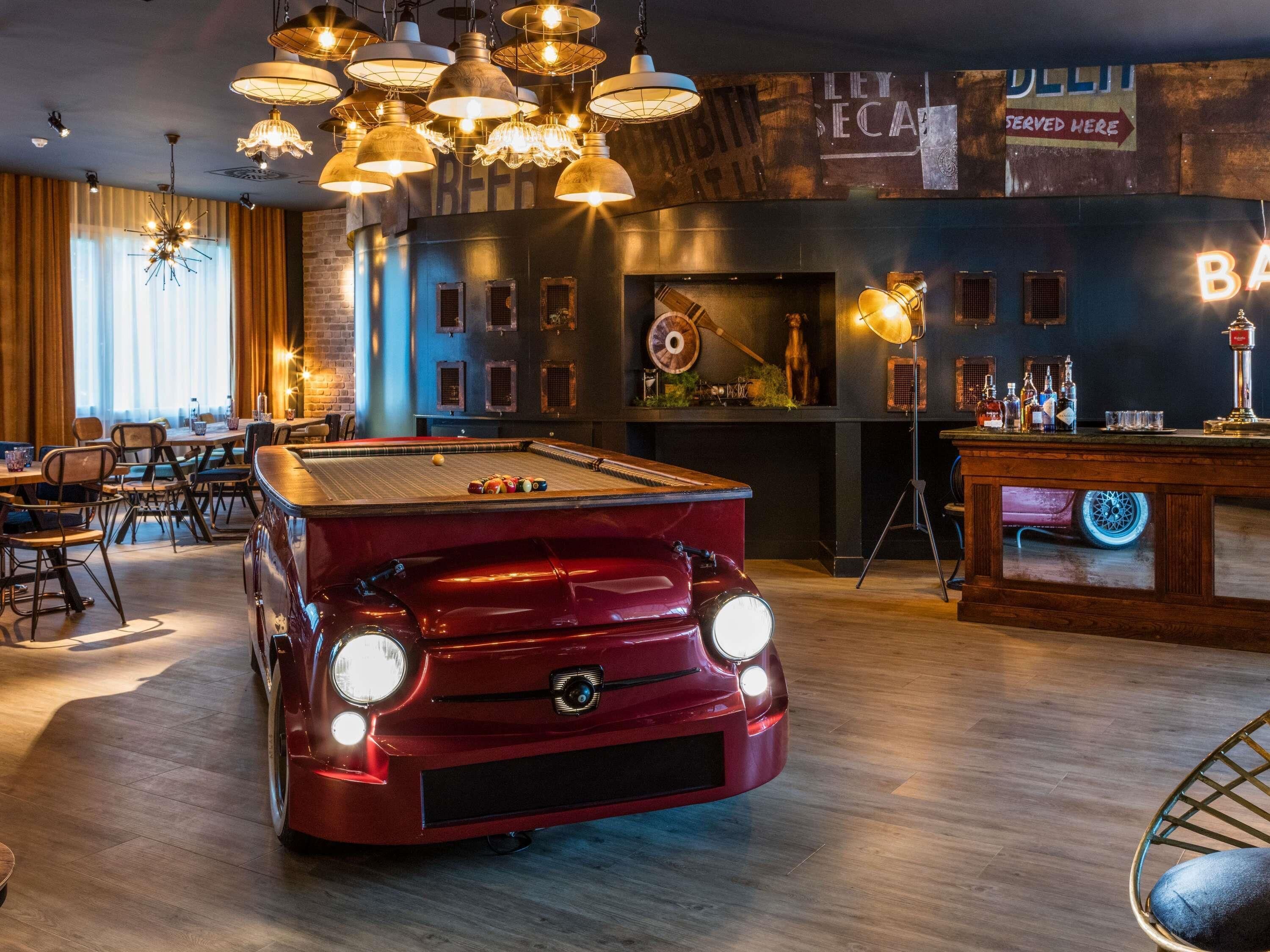 A billiards table in a bar setting with a vintage car model, wooden flooring, and hanging light fixtures.