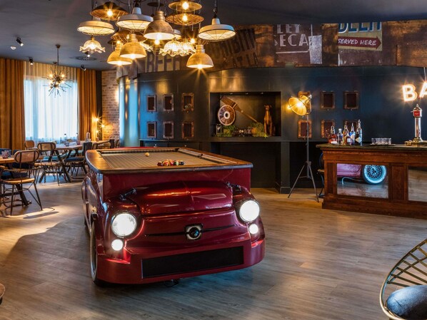 A billiards table in a bar setting with a vintage car model, wooden flooring, and hanging light fixtures. - Novotel Barcelona Cornella (Cornella de Llobregat)