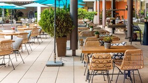 Un café al aire libre con mobiliario de mimbre, sombrillas azules y plantas en macetas.