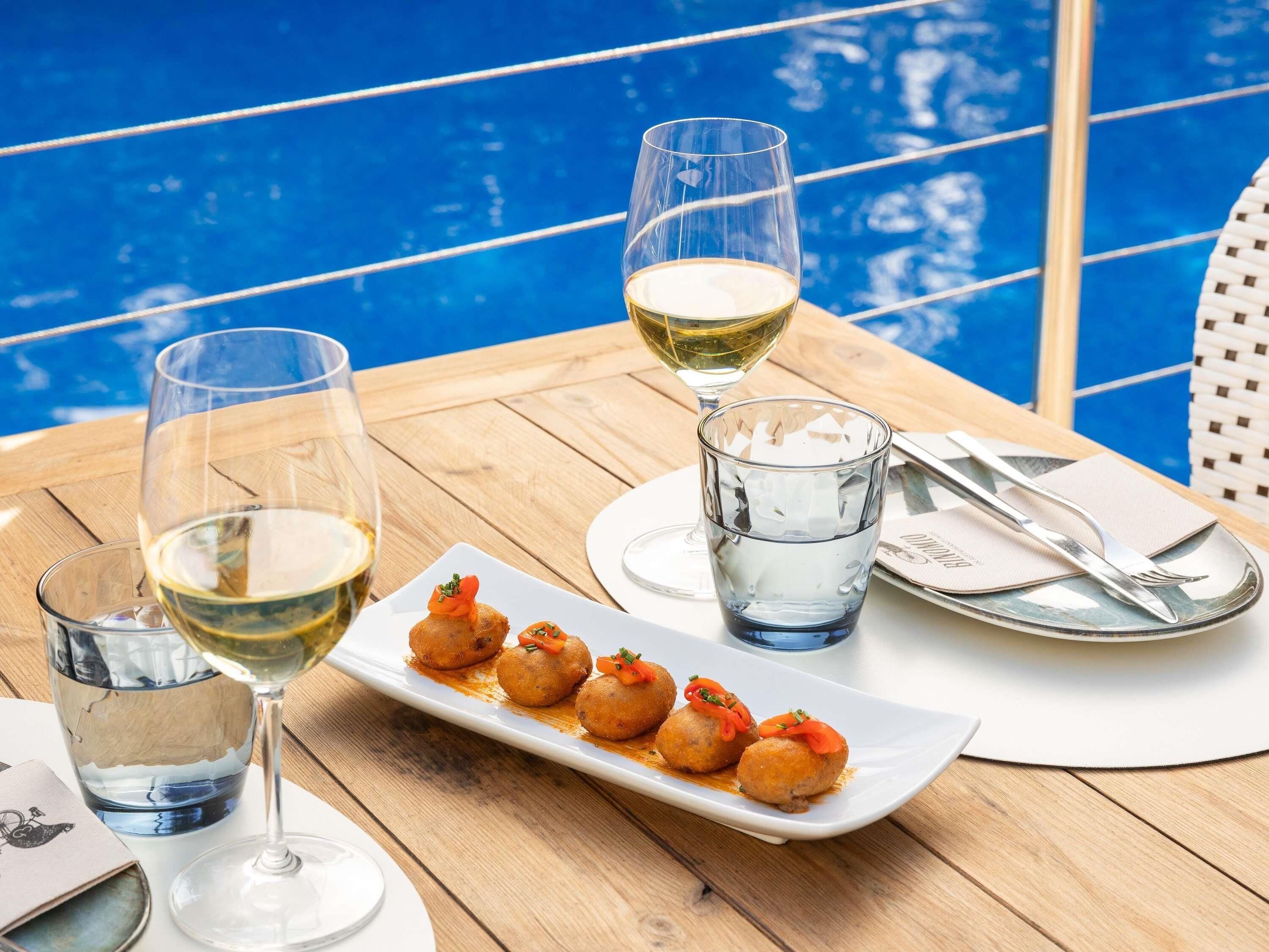 A dining table with a white plate of food, two glasses of white wine, and a clear glass of water.