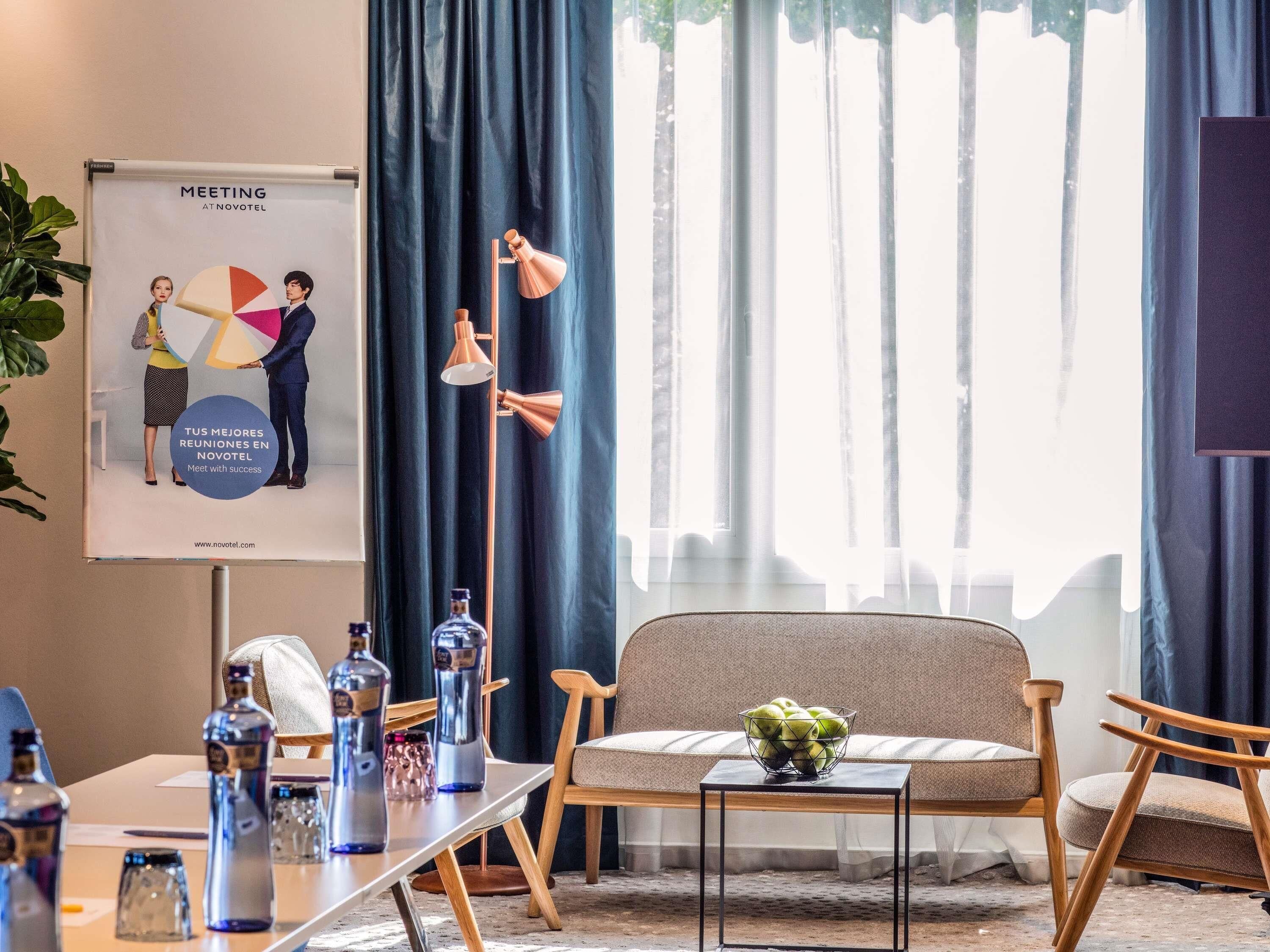 A meeting room with a projector screen displaying a presentation, a table with water bottles, and a sofa with a bowl of fruit.