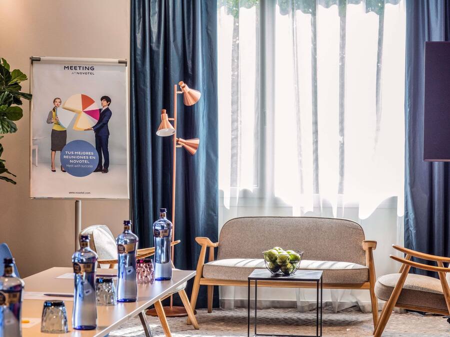 A meeting room with a projector screen displaying a presentation, a table with water bottles, and a sofa with a bowl of fruit.