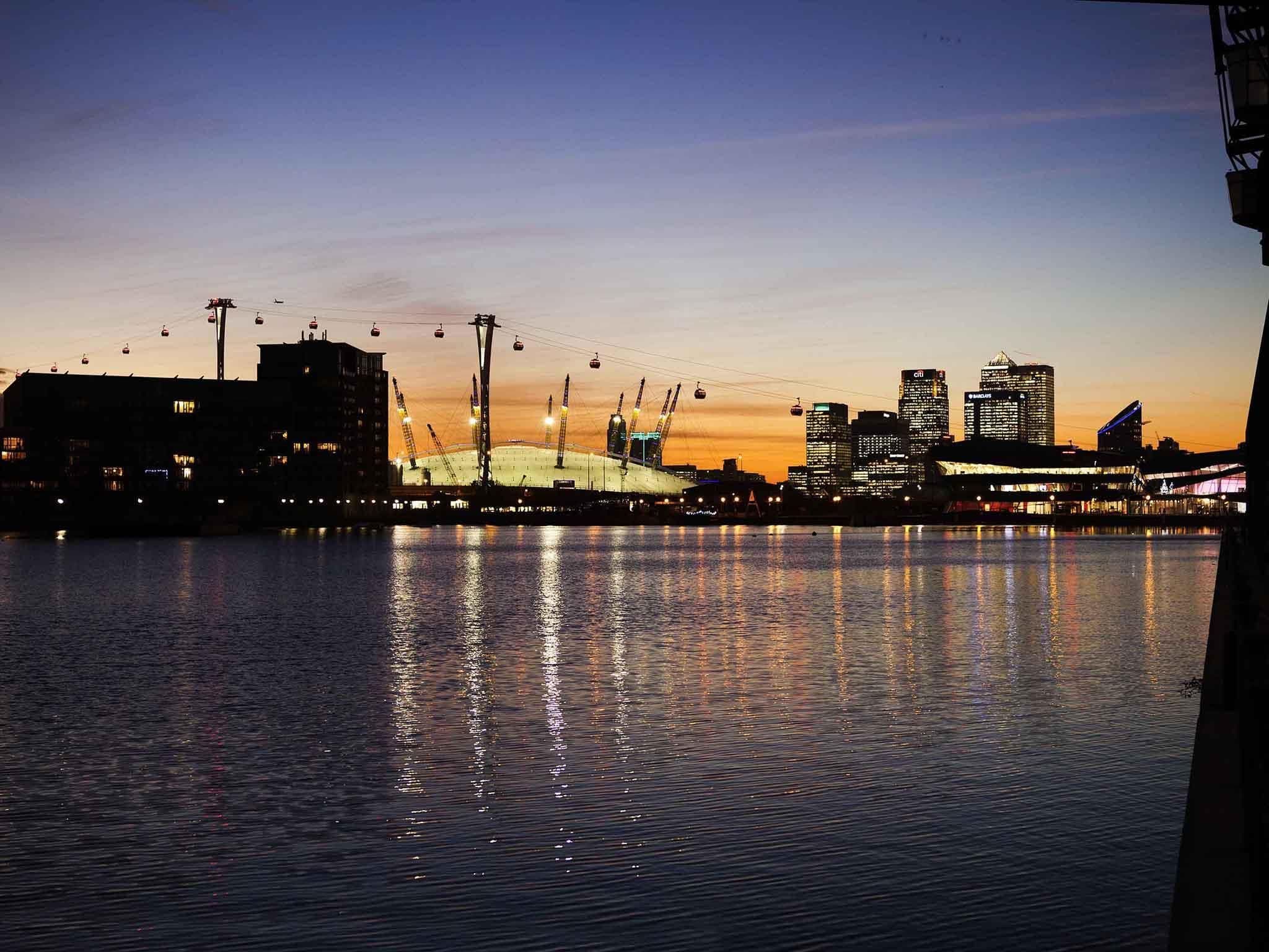 A waterfront cityscape with a bridge, buildings, and a body of water reflecting lights.