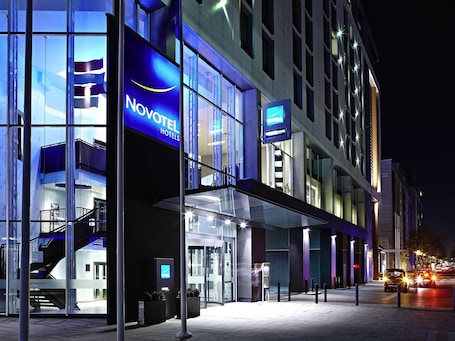 A modern hotel with a glass facade, a visible staircase, and a digital signboard.. Novotel London ExCeL
