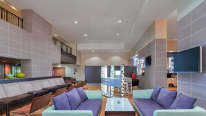 A modern lobby with seating areas, a reception desk, and a visible staircase.