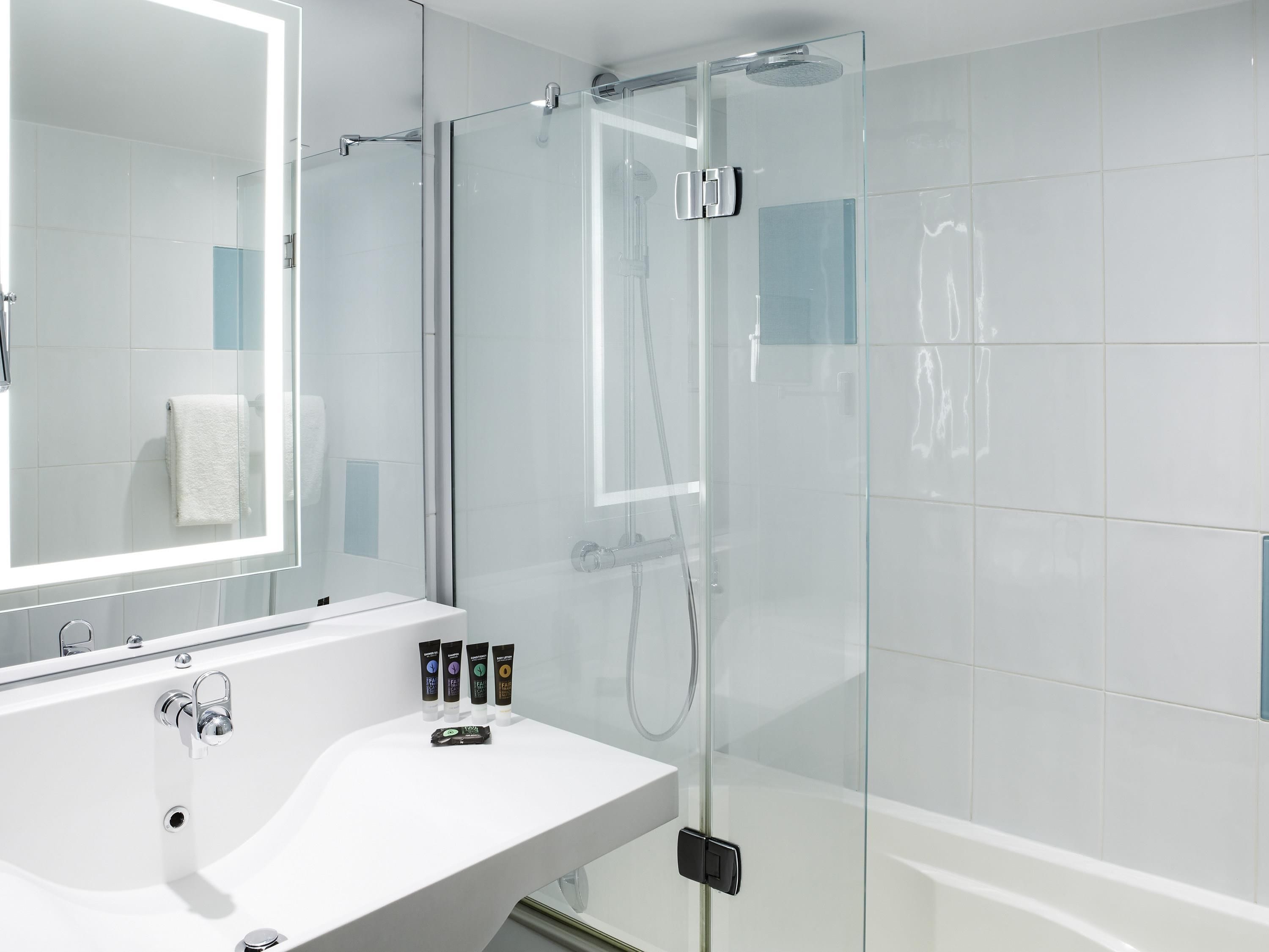 A modern bathroom with a glass-enclosed shower, a large mirror, and a white sink.
