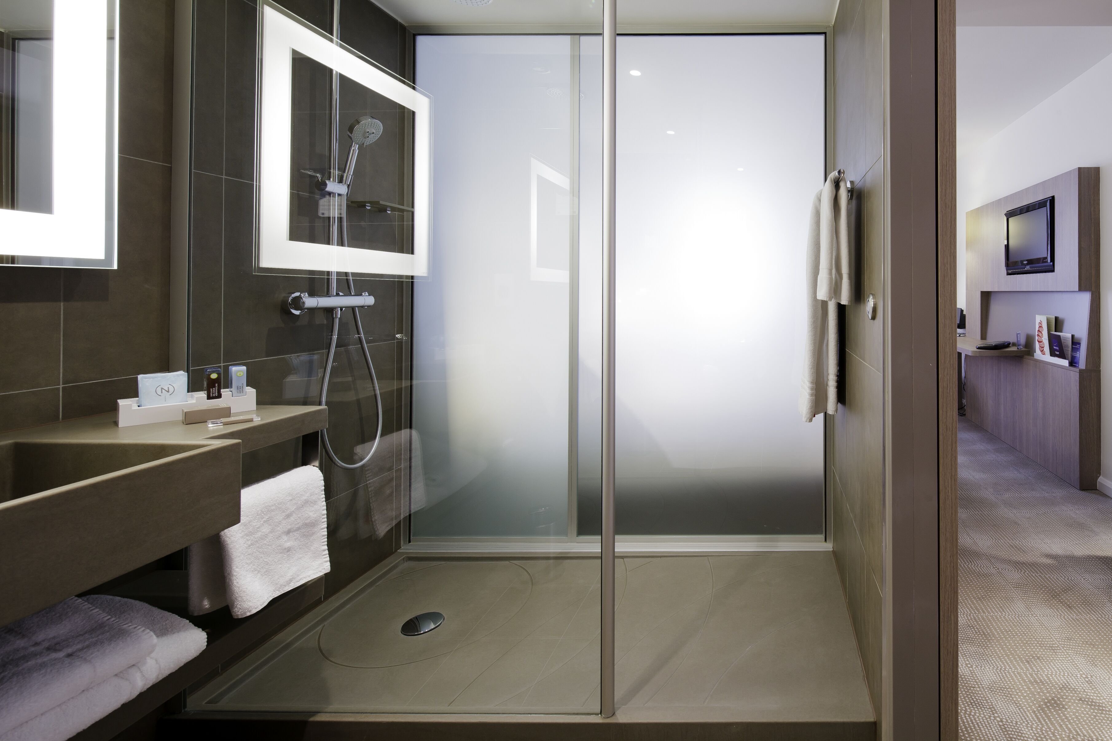 A modern bathroom with a glass-enclosed shower, a vanity with a mirror, and a towel rack.