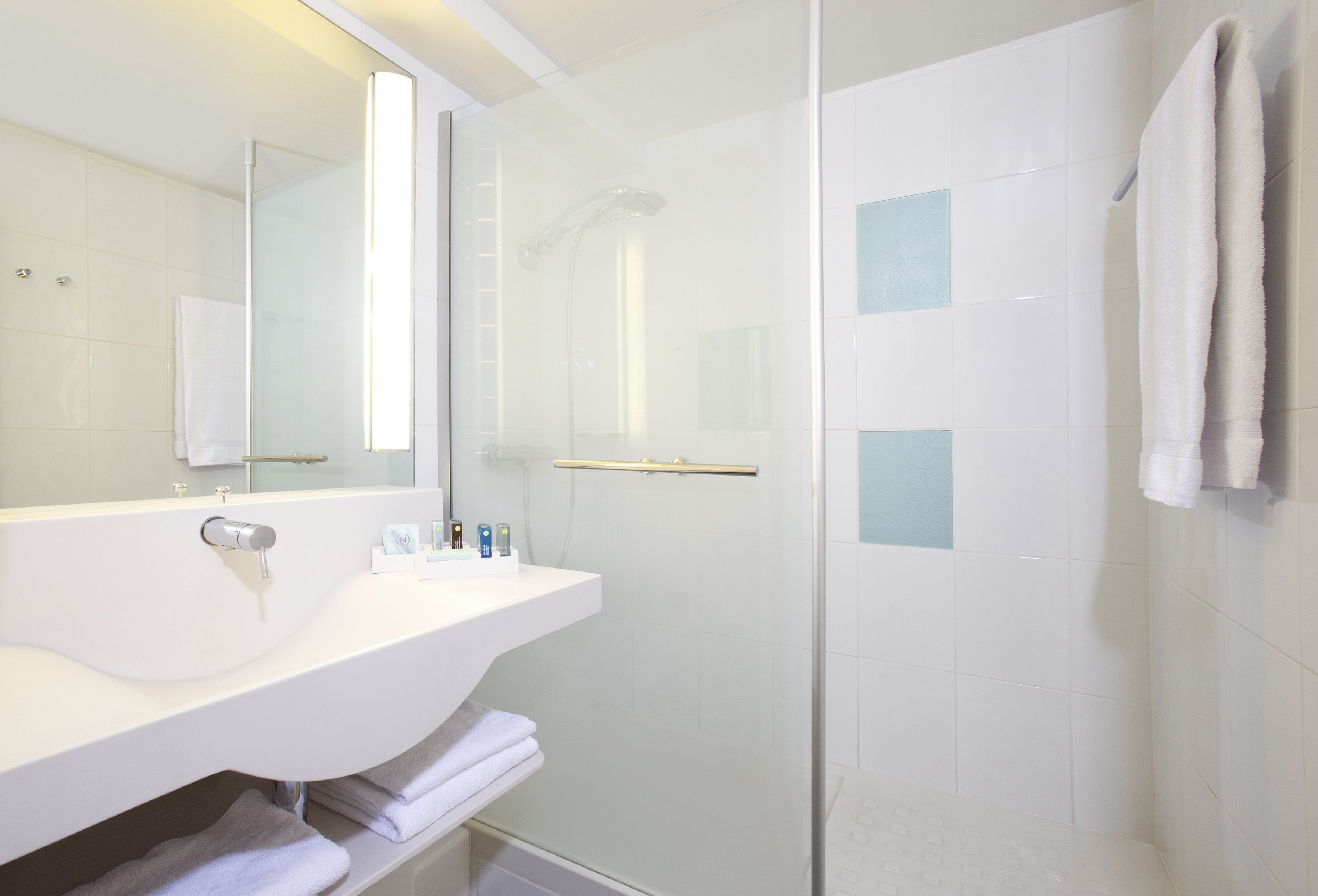 A modern bathroom with a glass-enclosed shower, a white sink with a mirror, and a towel rack.