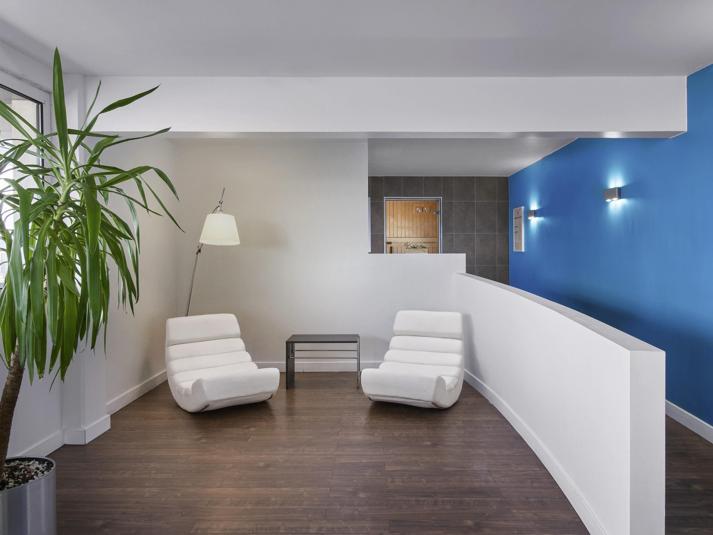 A modern waiting area with two white chairs, a floor lamp, and a large potted plant.
