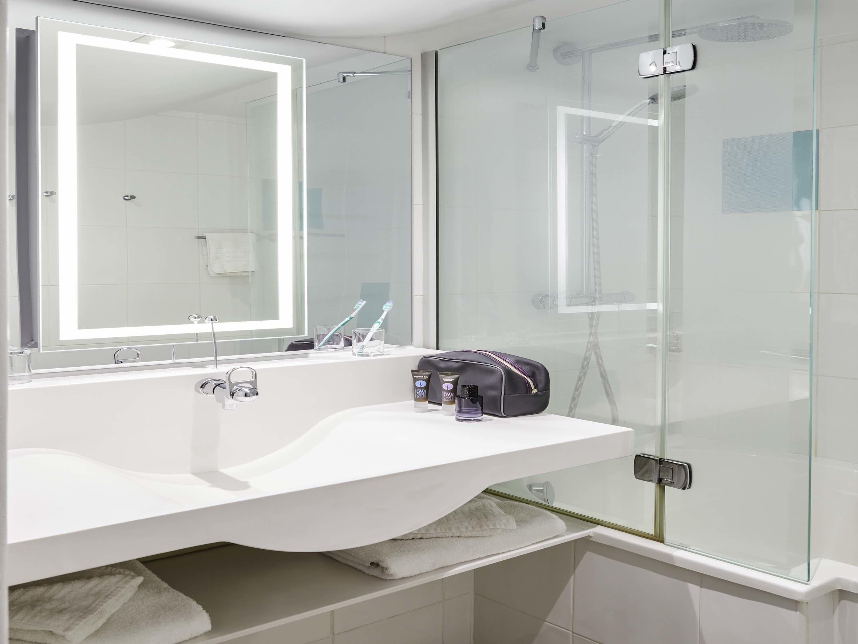 A modern bathroom with a glass-enclosed shower, a white sink with a mirror, and toiletries on the counter.