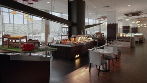 A modern restaurant with a central island counter, white chairs, and a large window with a view of the cityscape.