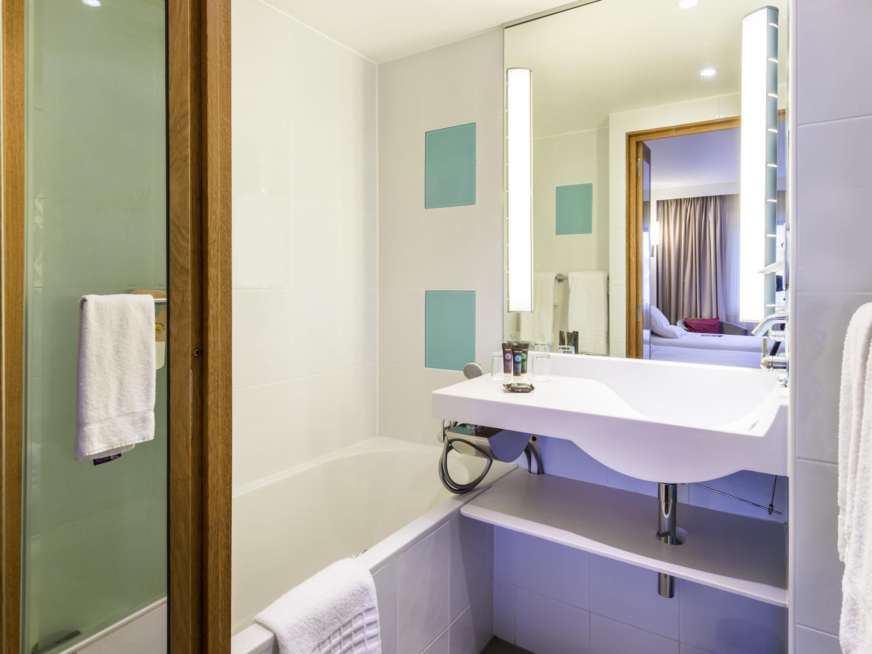 A modern bathroom with a glass shower enclosure, a white bathtub, and a vanity with a mirror.