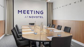 A meeting room with a large table, chairs, and a wall with 'MEETING AT NOVOTEL' text.