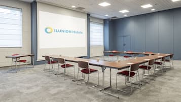 Una sala de conferències amb una taula llarga, cadires i una pantalla de projecció que mostra el logotip d'Ilunion Hotels.