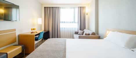 Habitación de hotel con una cama grande, un escritorio con una silla, televisión y ventana con cortinas.