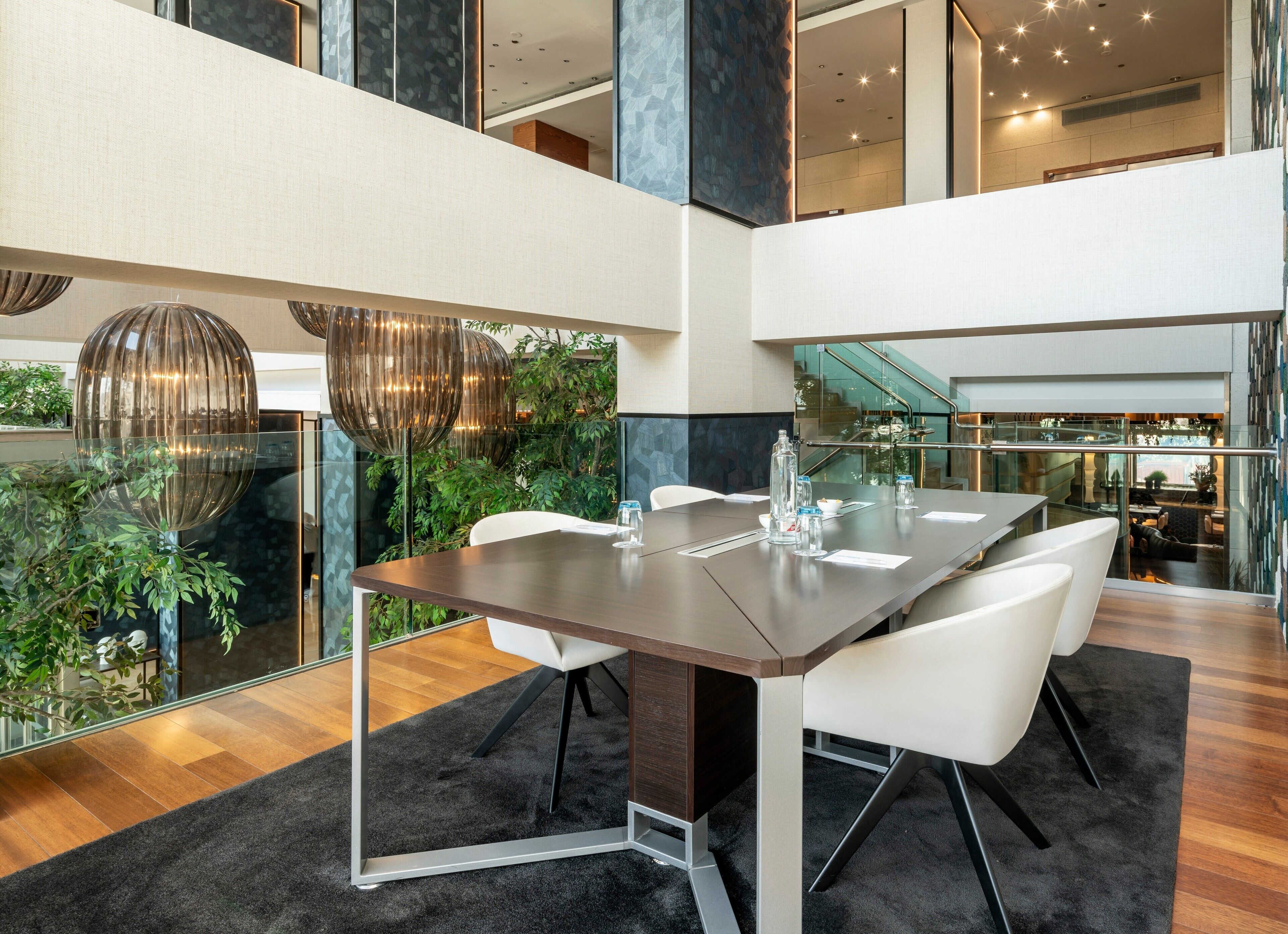 Una sala de conferencias moderna con una mesa de cristal, sillas blancas y vistas a plantas de interior.