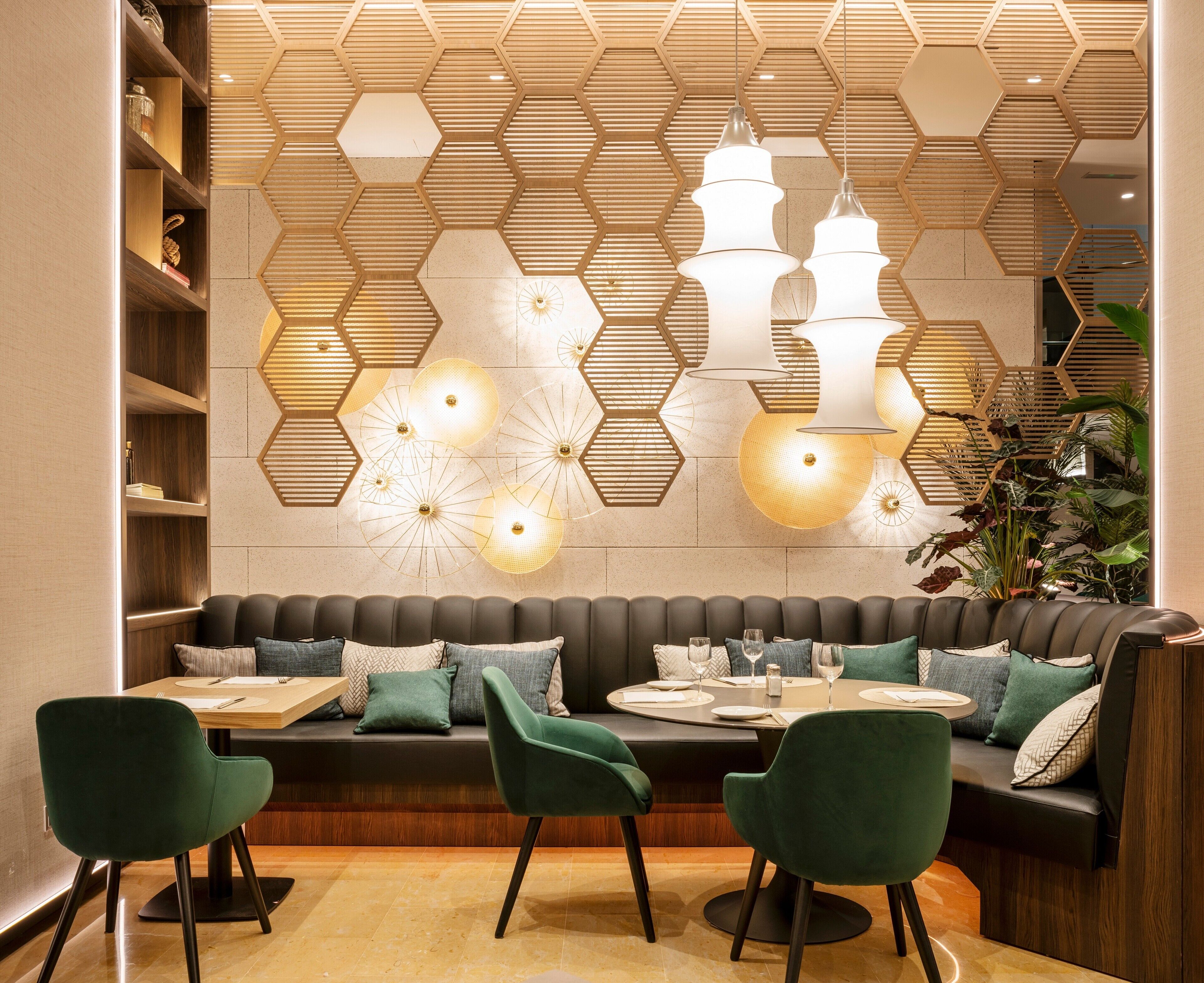 A modern dining area with a wooden hexagonal ceiling design, a dark sofa with green chairs, and a table set for two.