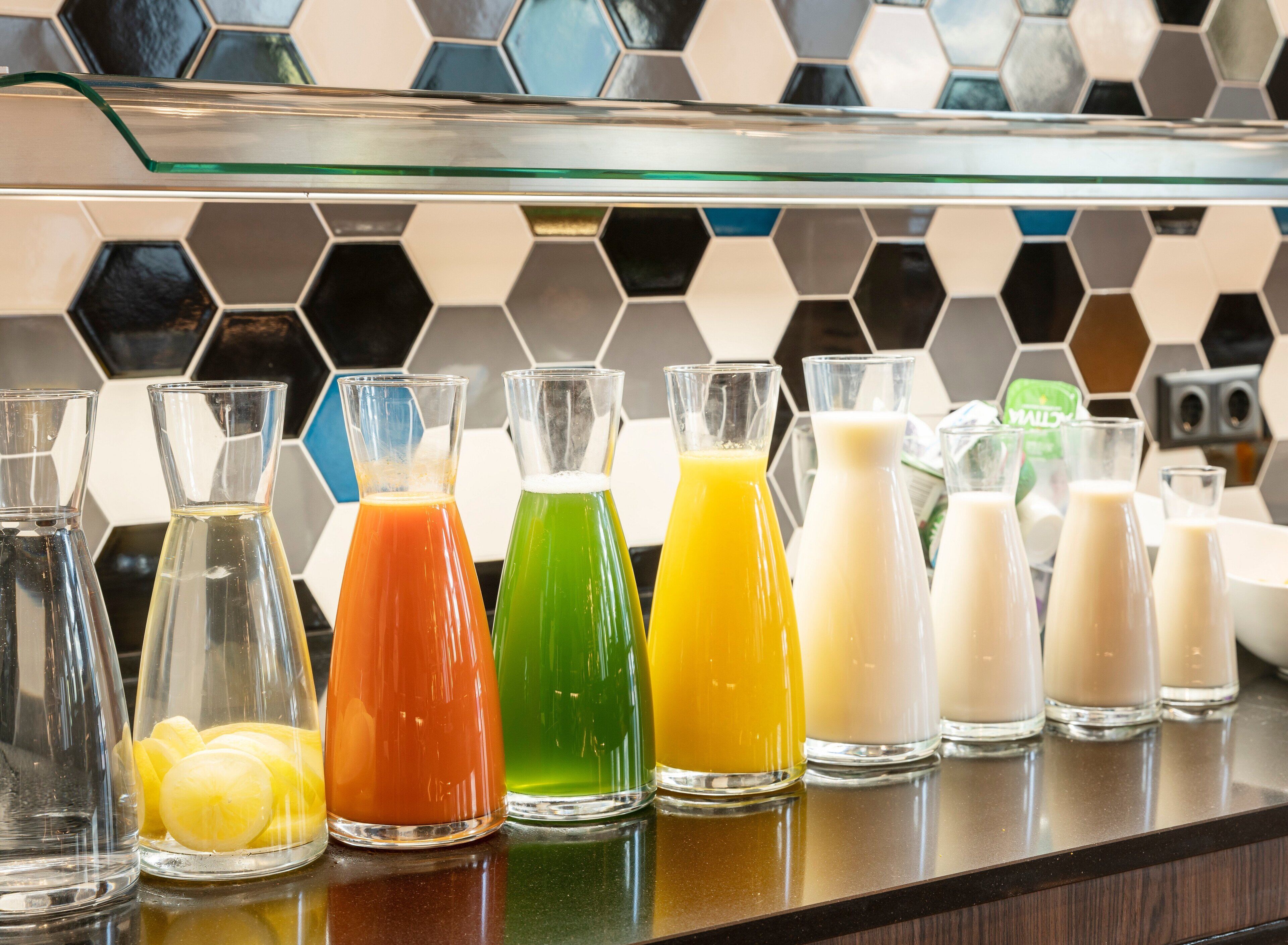 Una encimera de cocina con varias botellas de vidrio que contienen líquidos coloridos, probablemente zumos o batidos, y un salpicadero con diseño de panal.