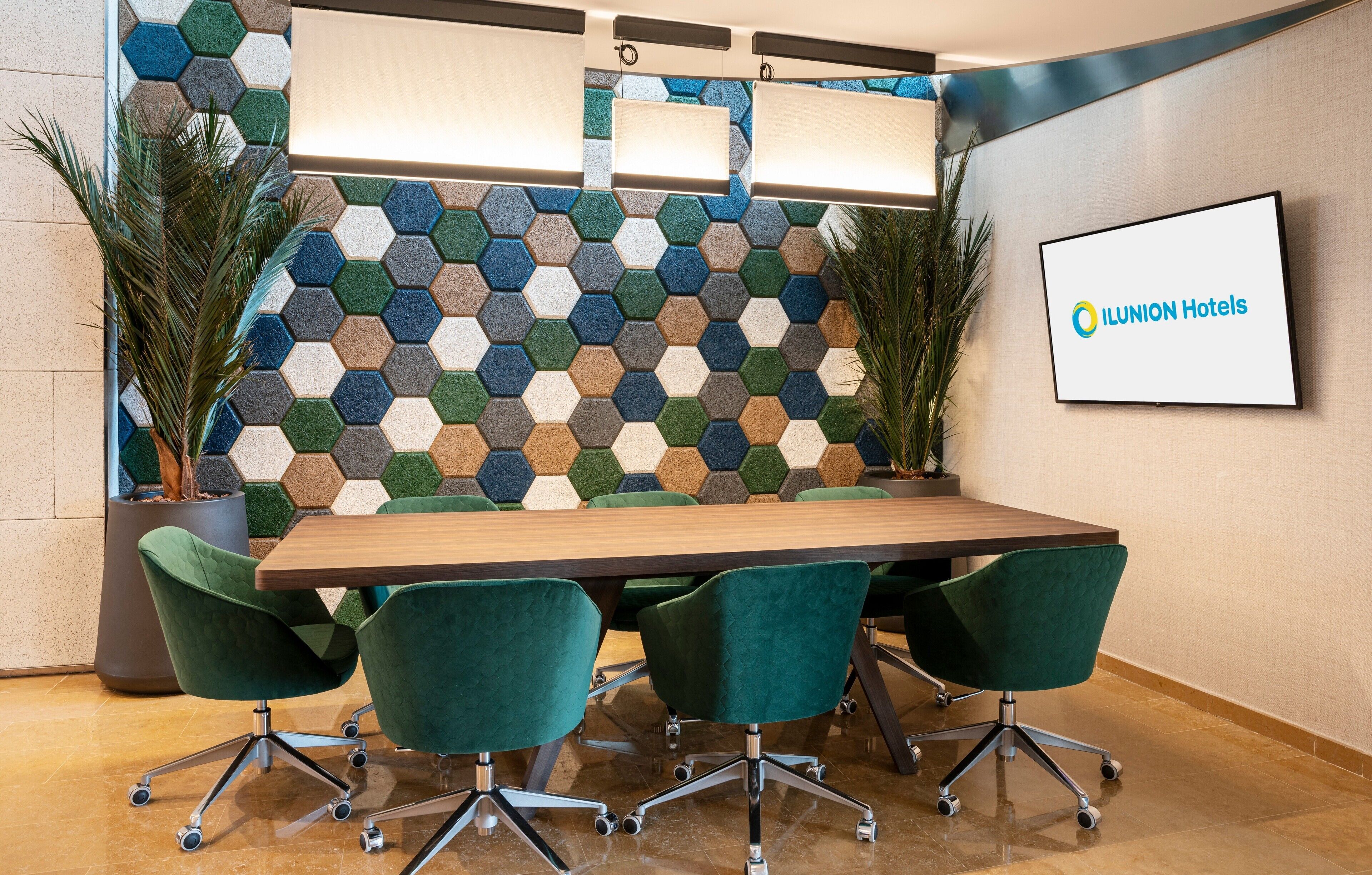 A conference room with a hexagonal patterned wall, a wooden table, and green upholstered chairs.