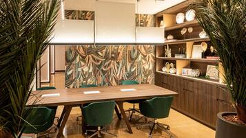 A conference room with a long table, green chairs, a whiteboard, and a decorative wall with a leaf pattern.