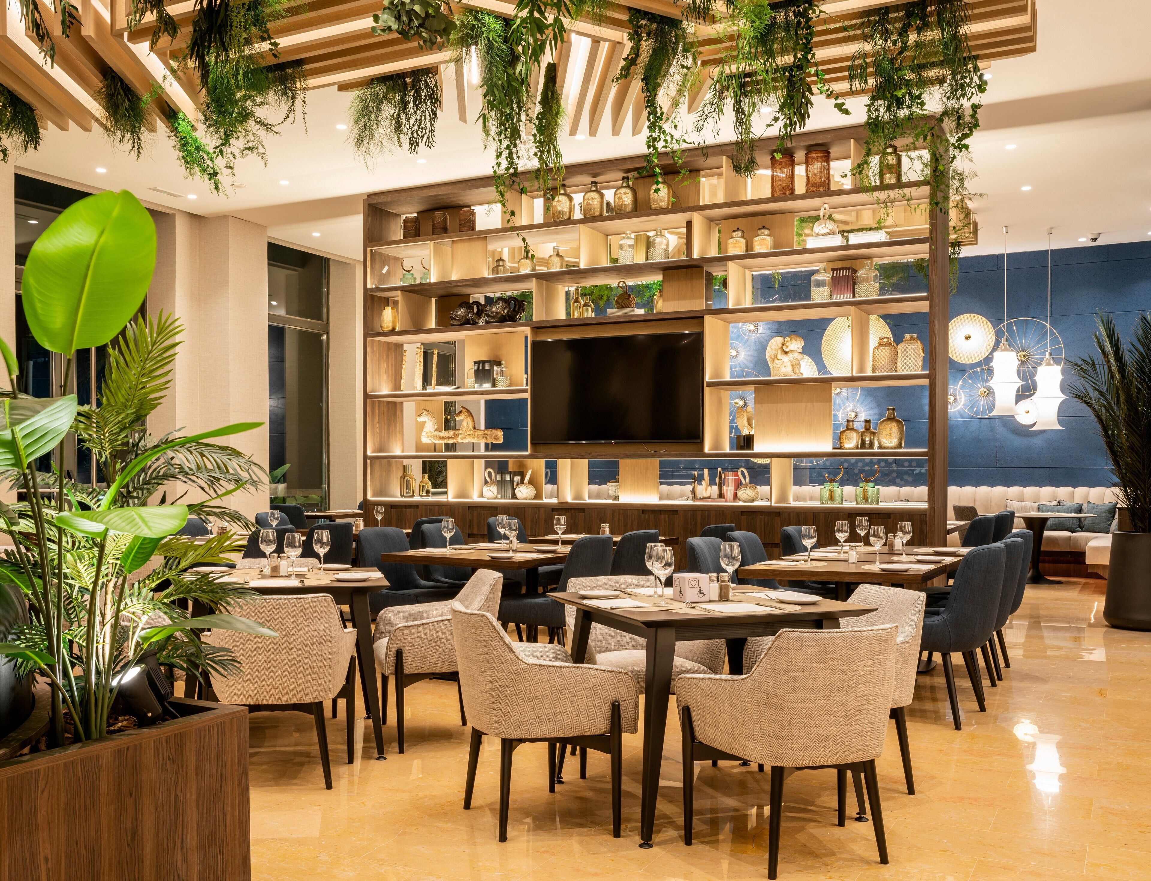 Un restaurante con varias mesas y sillas, una televisión grande y estanterías con diversos objetos.