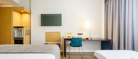 Habitación de hotel con dos camas, un escritorio, una silla, un televisor, una lámpara y un minibar.