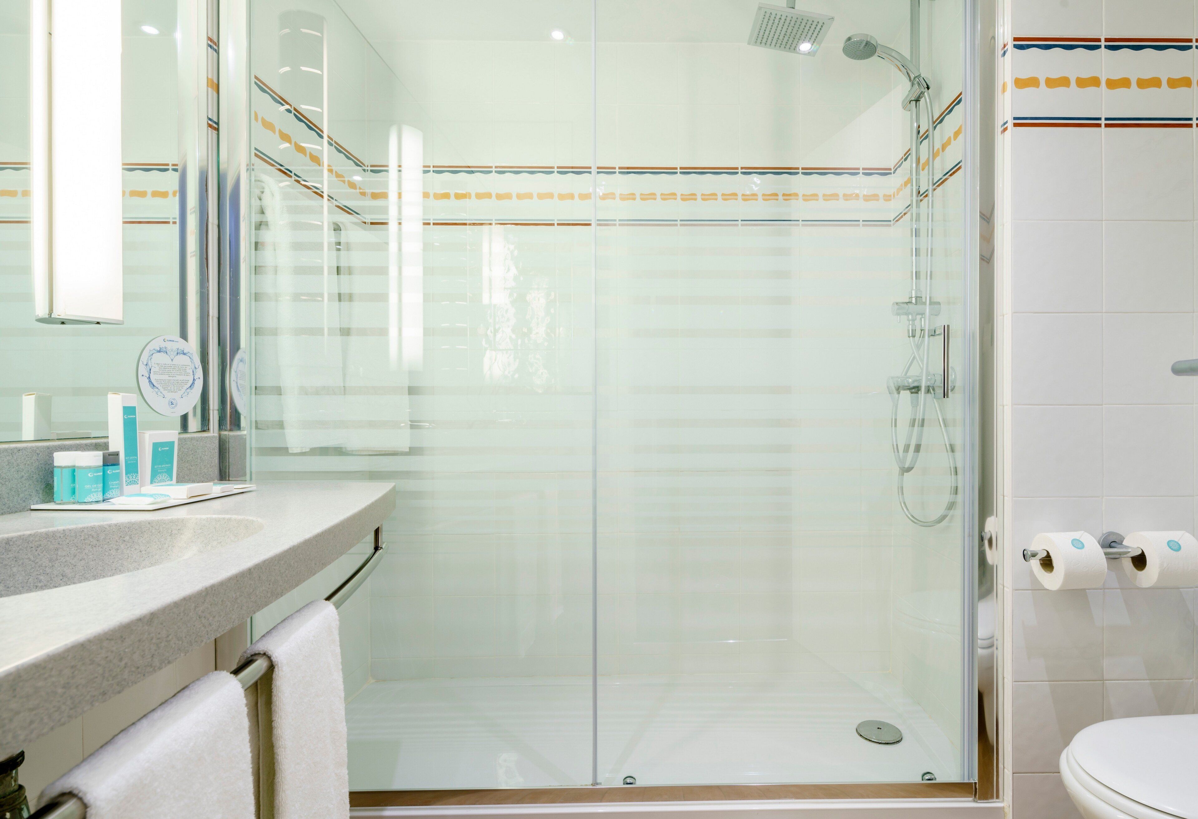 Un baño moderno con cabina de ducha de vidrio, tocador con artículos de aseo y inodoro con papel higiénico.