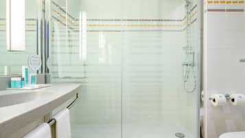 Un baño moderno con cabina de ducha de vidrio, tocador con artículos de aseo y inodoro con papel higiénico.