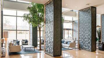 Un vestíbulo moderno con grandes ventanales, un árbol y zonas de estar.